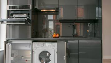 Una cocina compacta con electrodomésticos integrados, incluyendo una lavadora y un lavavajillas, y una pequeña encimera.