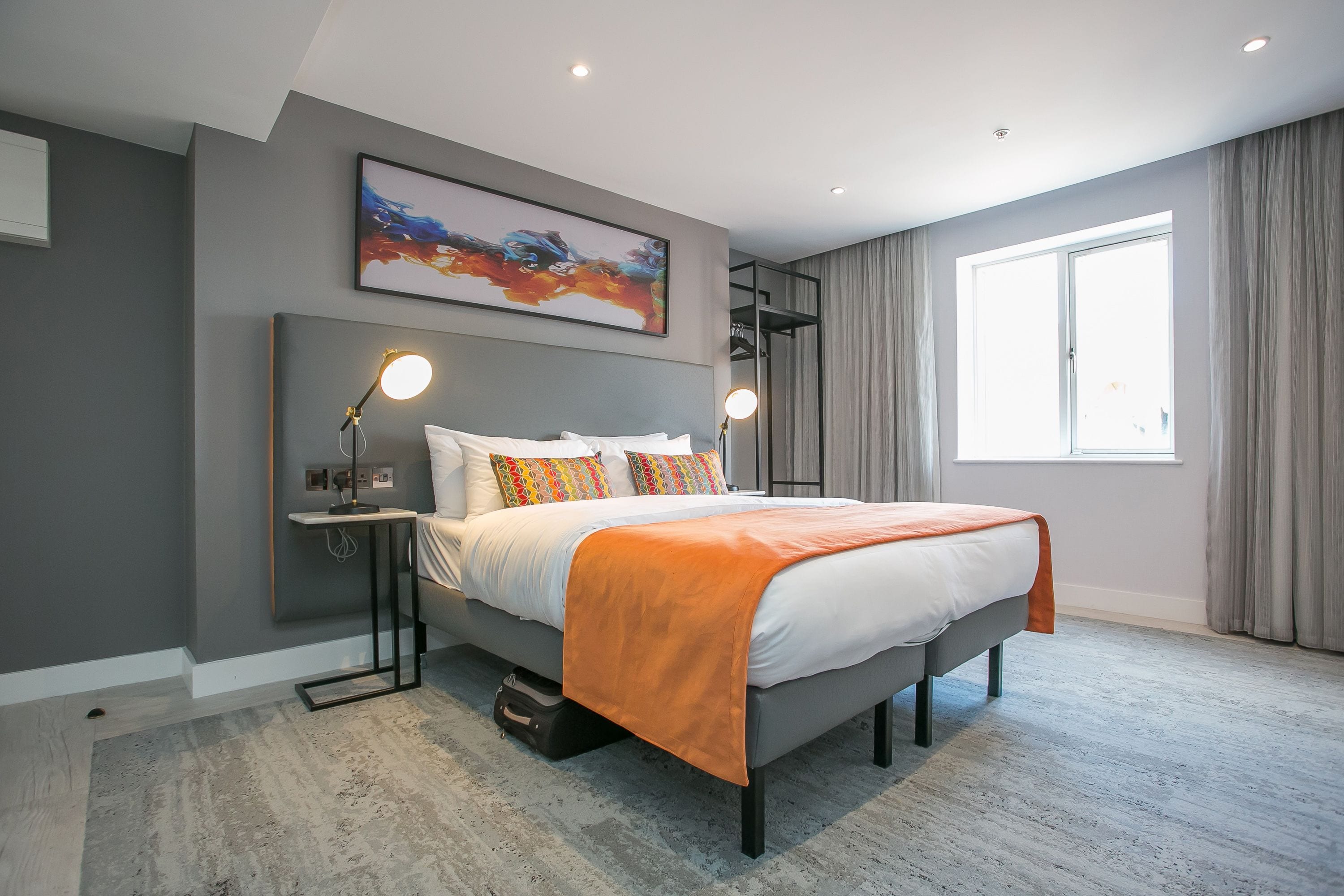 Un dormitorio moderno con una cama, lámparas de noche, un cuadro y una ventana con cortinas.