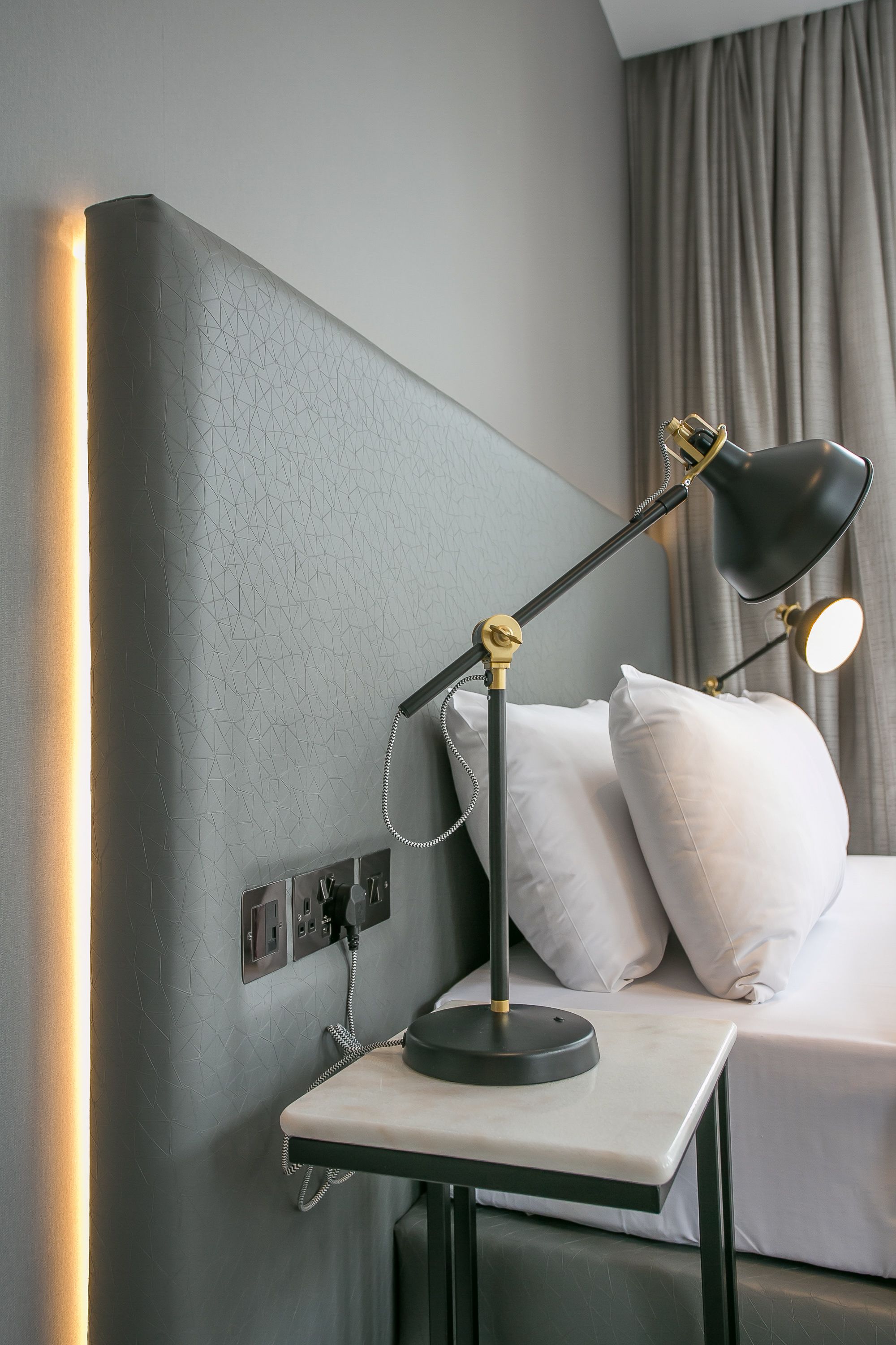 Un lit bien fait, avec des oreillers blancs et une table de chevet sur laquelle se trouve une lampe.