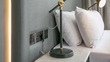 Un lit bien fait, avec des oreillers blancs et une table de chevet sur laquelle se trouve une lampe.