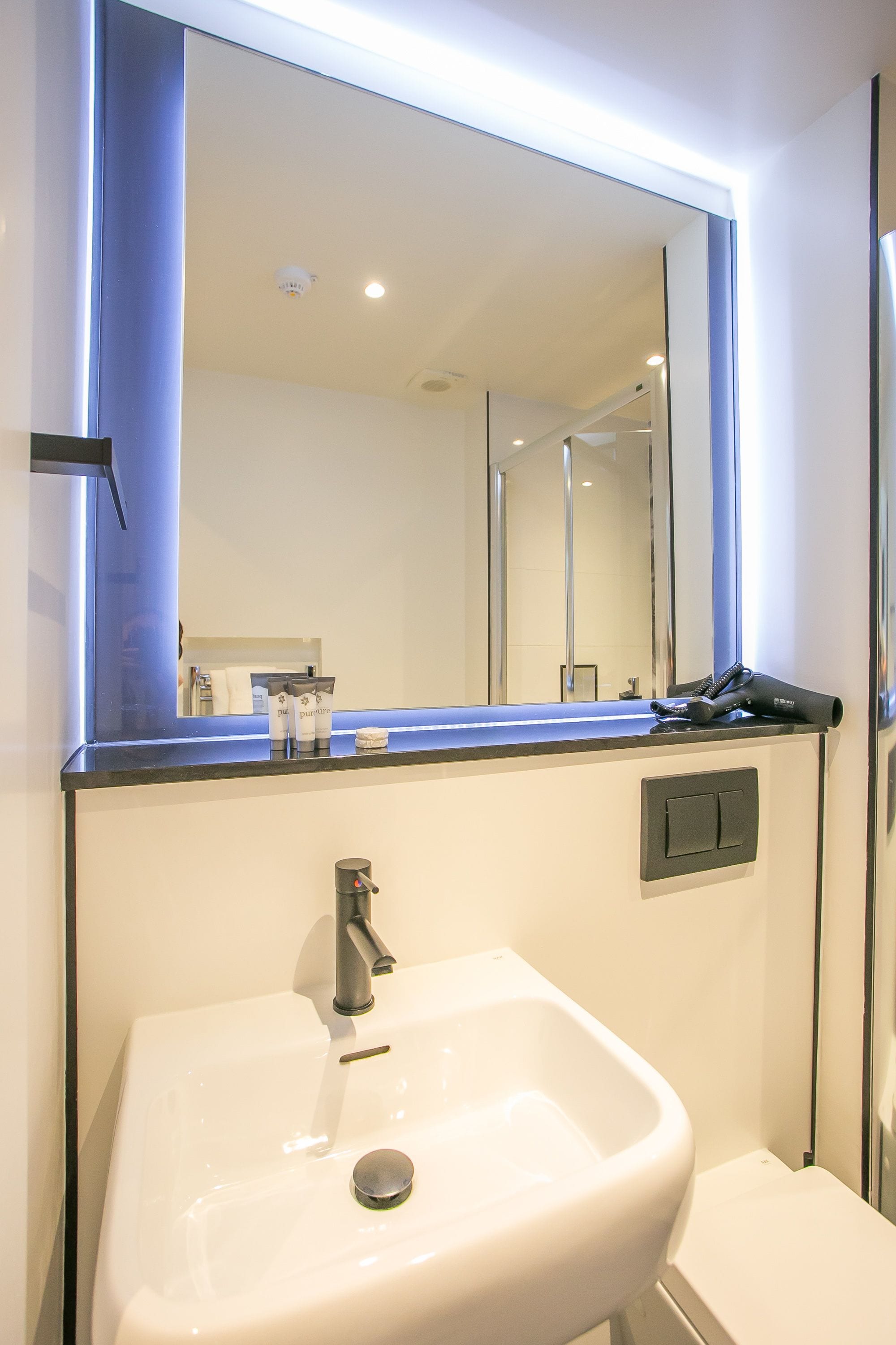 A bathroom with a white sink, a mirror, and a hairdryer on the counter.