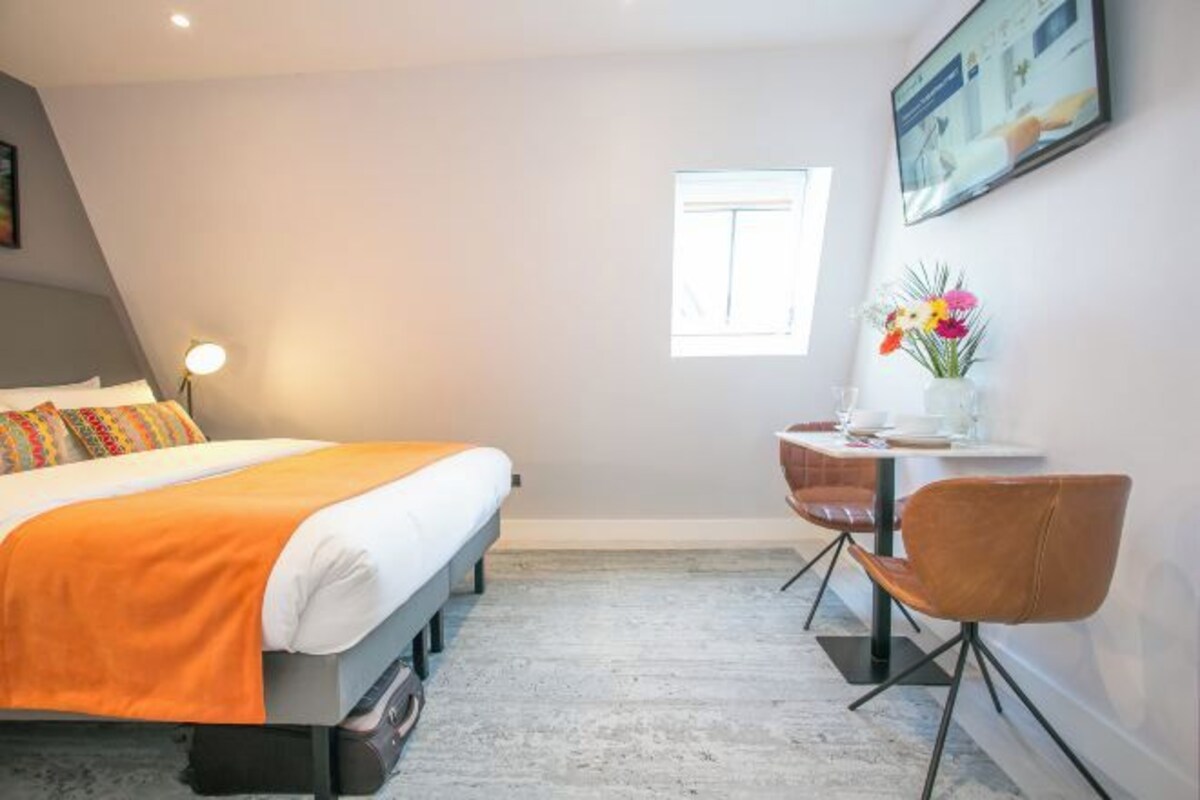 A bedroom with a bed, a desk, a chair, a lamp, and a window.