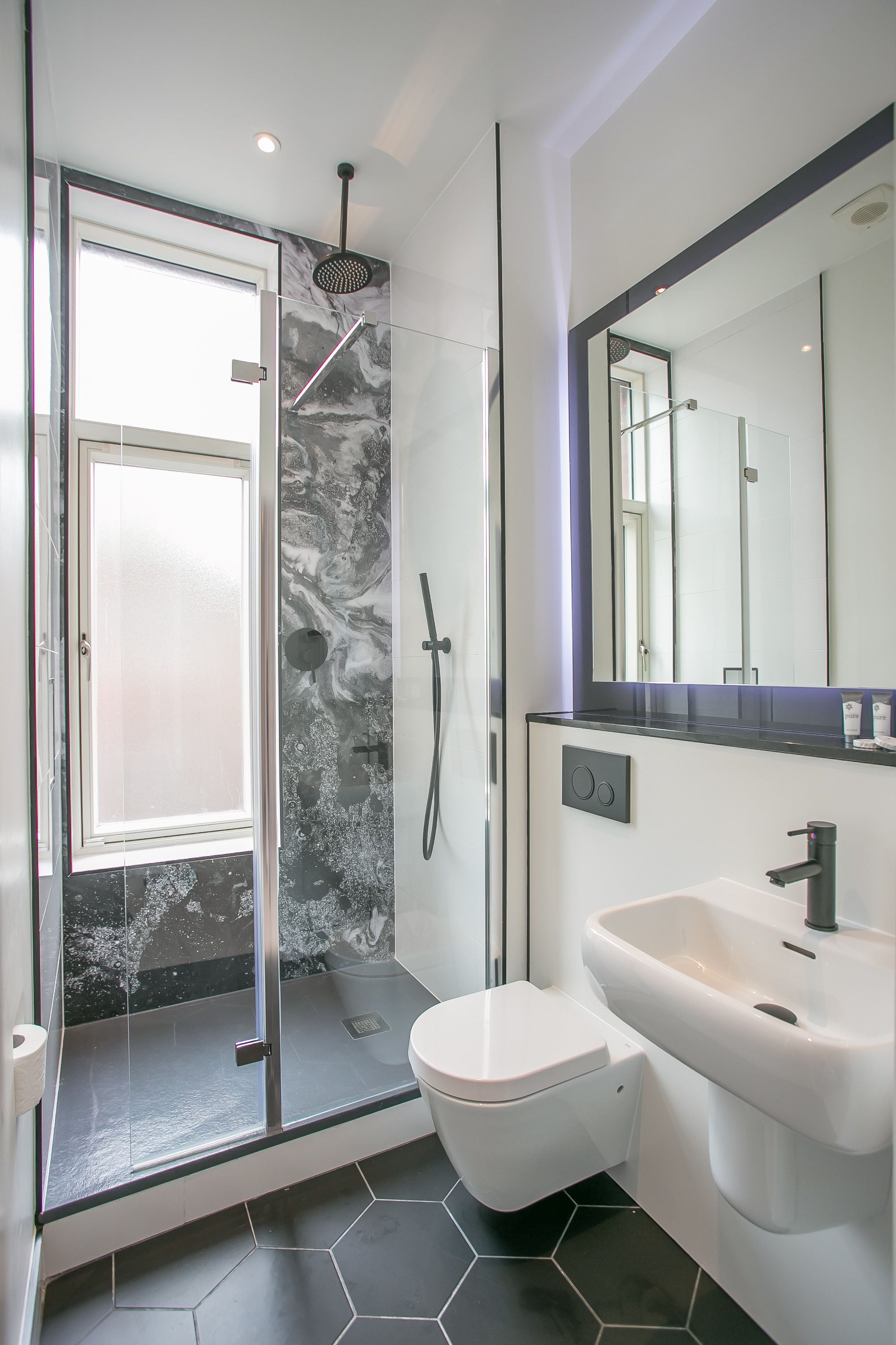 A modern bathroom with a glass-enclosed shower, a white toilet, and a large mirror above the sink.