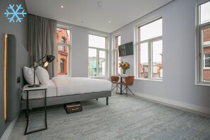A modern bedroom with a bed, bedside table, lamp, and a view of a brick building through large windows. - Grafton Street Boutique Aparthotel by City Break Apartments (Dublin)