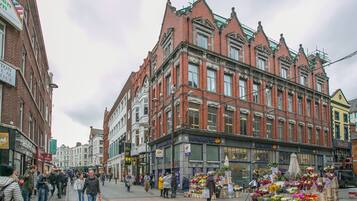 A street with a row of red brick buildings, a flower market, and pedestrians.