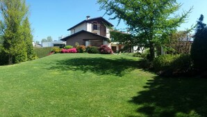 A house with a sloped roof, surrounded by a well-maintained lawn and various shrubs. - B&B Casa Ceruti (Villa Guardia)