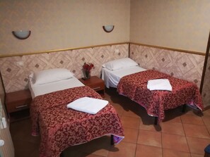 A hotel room with two beds, each with a red patterned bedspread and white pillows. There is a nightstand with a vase of red flowers between the beds. The room has a patterned wallpaper and a tiled floor. - Cristina's Residence (Rome)