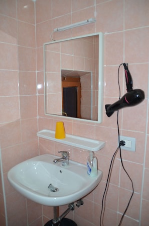 A bathroom with a white sink, mirror, and a hairdryer mounted on the wall. - Cristina's Residence (Rome)