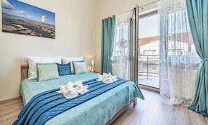 Cama bem arrumada com colcha azul, arranjo de travesseiros e toalha sobre a cama.