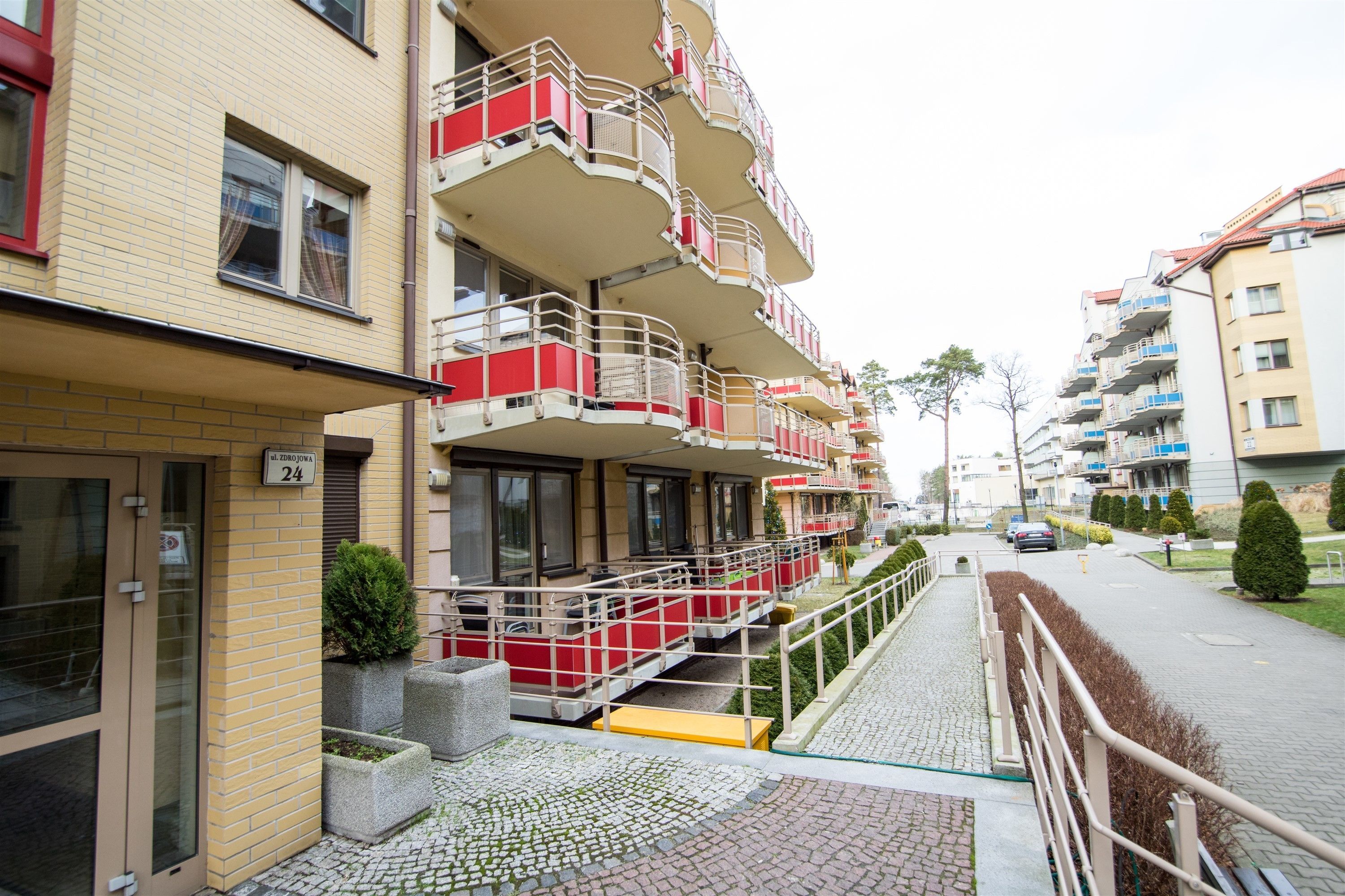 A multi-story hotel with balconies, a paved walkway, and a street view.