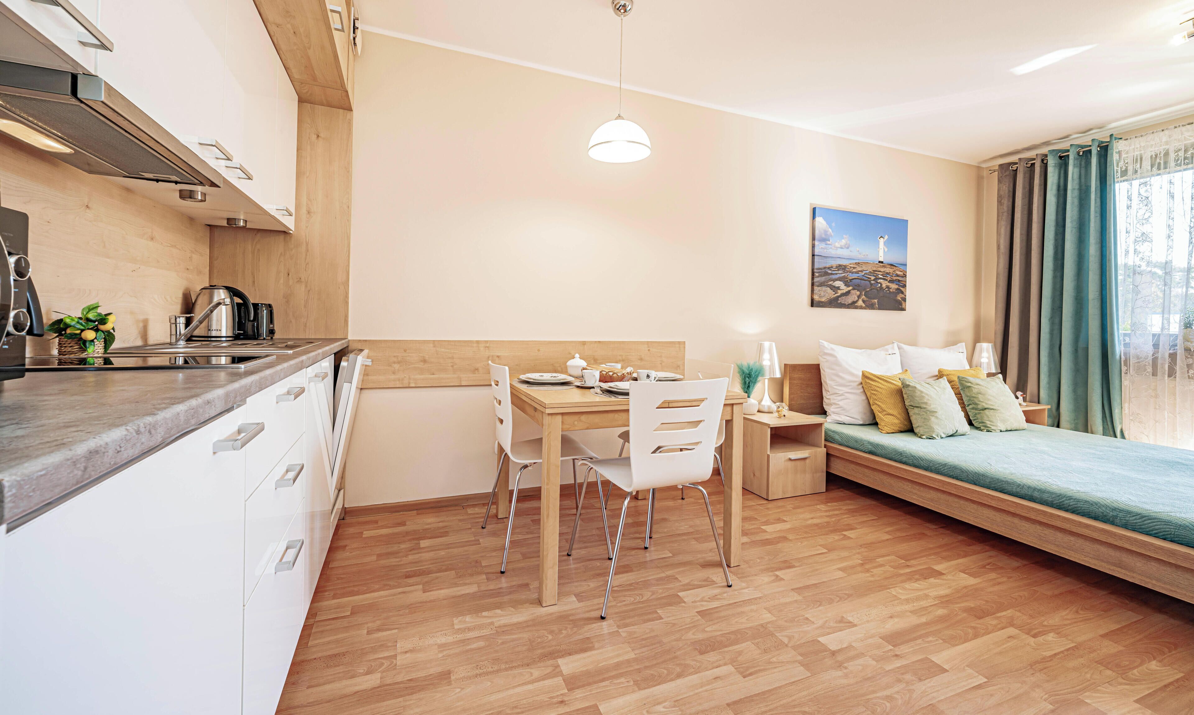 A modern kitchen with a dining area, a bed with a view, and a painting on the wall.