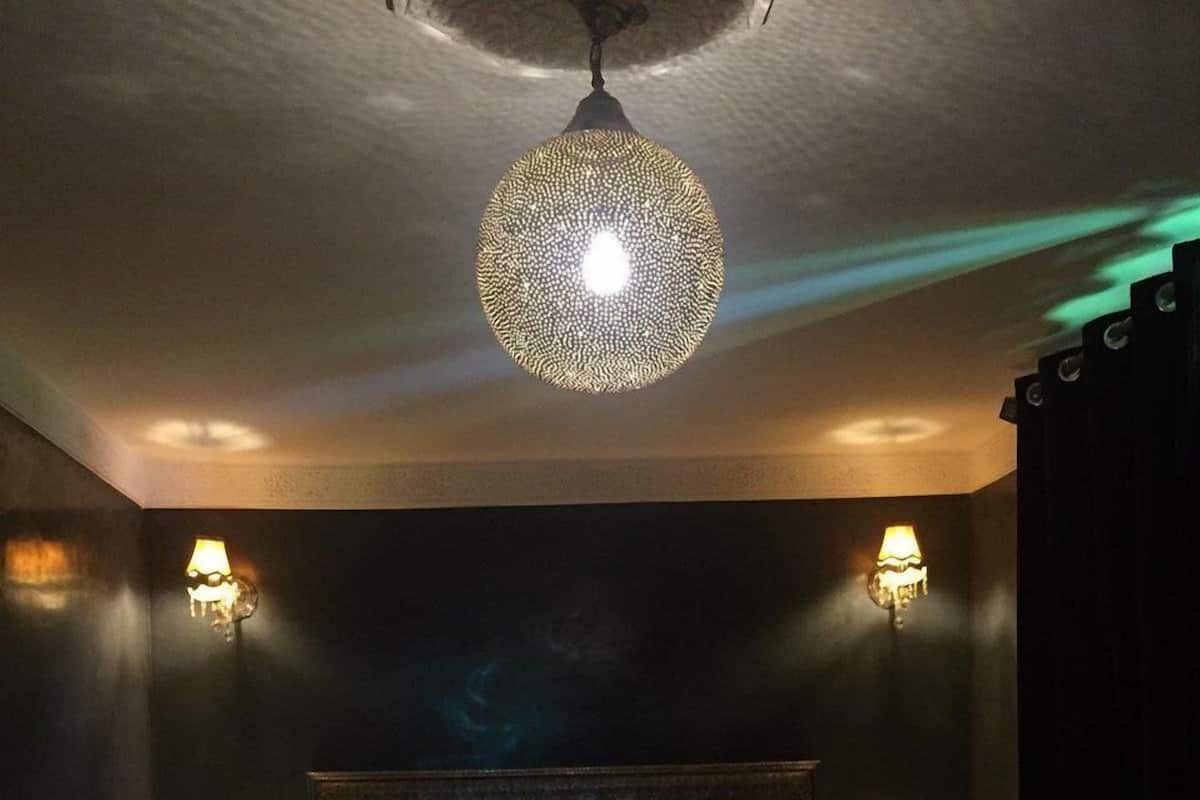 A hotel room with a large bed, two bedside lamps, a decorative ceiling light, and a dark-colored headboard.