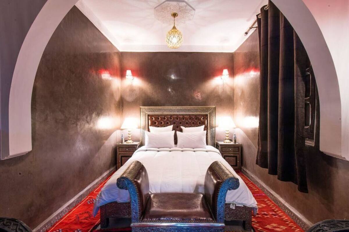 A bedroom with a large bed, two bedside lamps, a decorative ceiling light, and a red carpet.