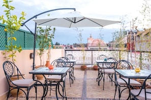Un patio al aire libre con mesas y sillas, plantas en macetas y vista a un edificio al fondo.
