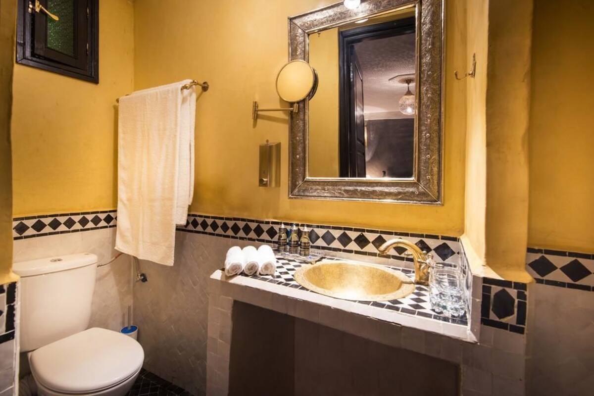 A bathroom with a white toilet, a sink with a marble countertop, and a mirror with a gold frame.