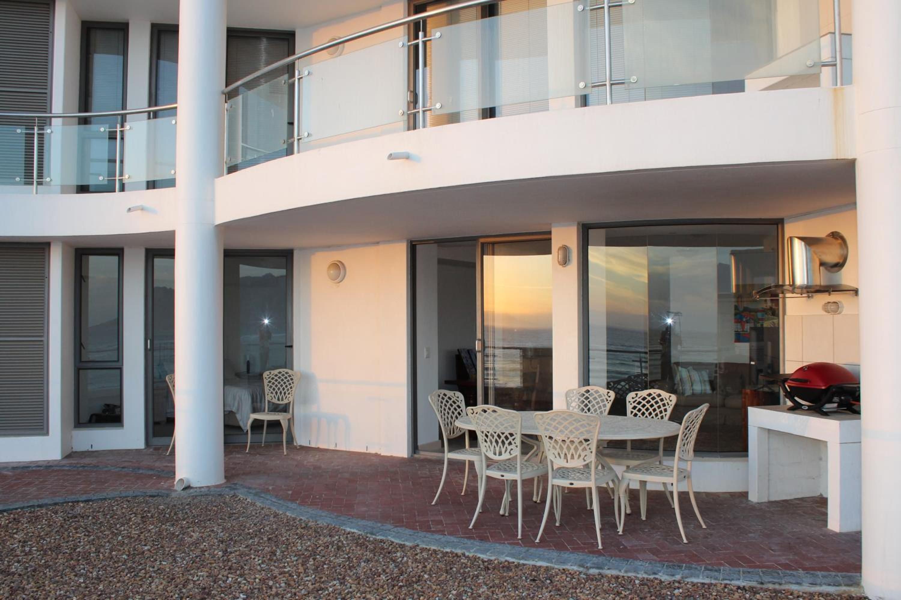 A modern outdoor patio with a round table and chairs, a grill, and a view of the sea.