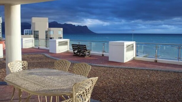 An outdoor terrace with a table and chairs, a bench, and a view of the ocean and mountains.