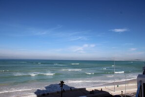 Une vue sur la côte, avec un ciel dégagé, des vagues et une promenade piétonne longeant la plage.