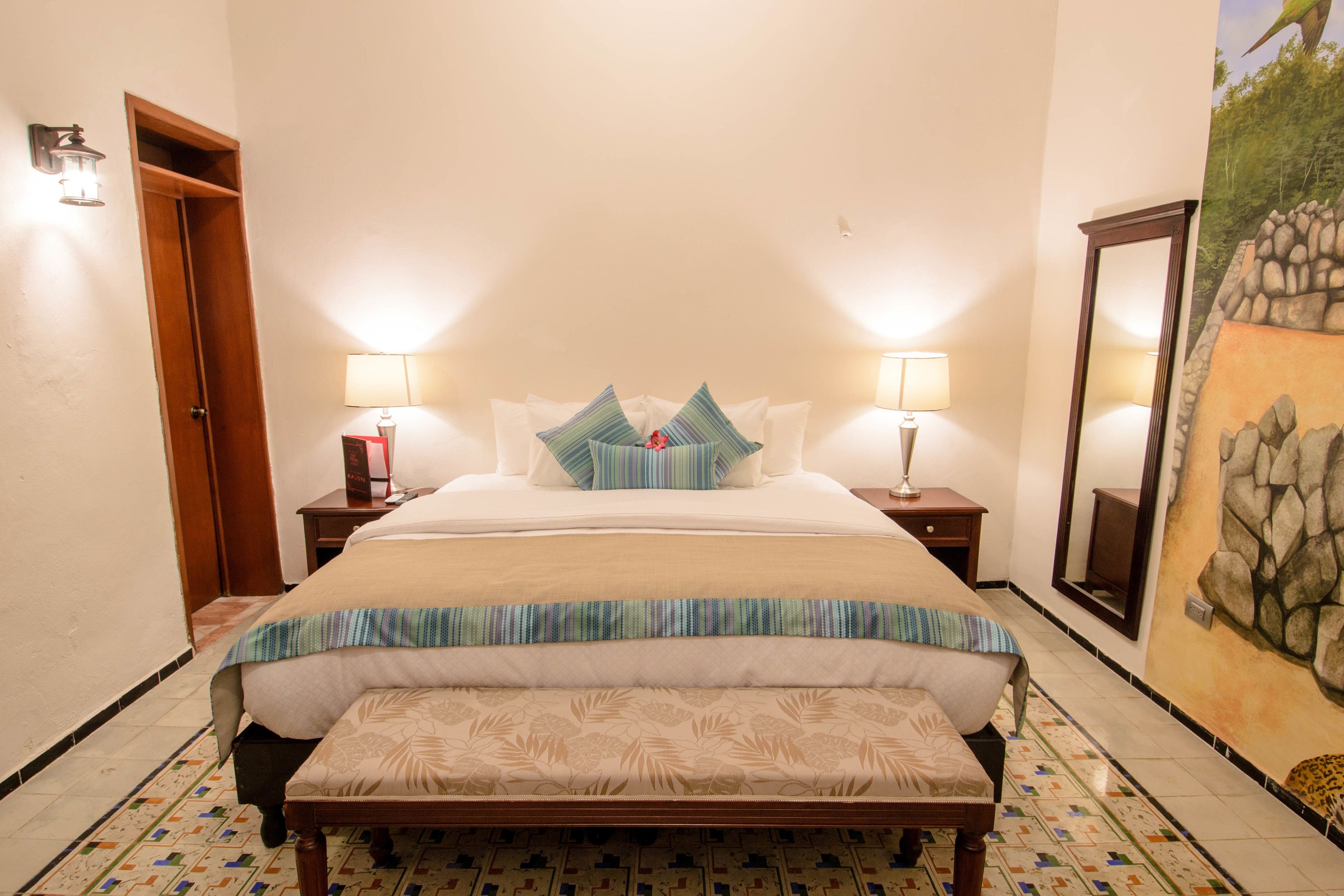 Une chambre bien rangée, avec un lit, des tables de chevet, un banc et un miroir fixé au mur.