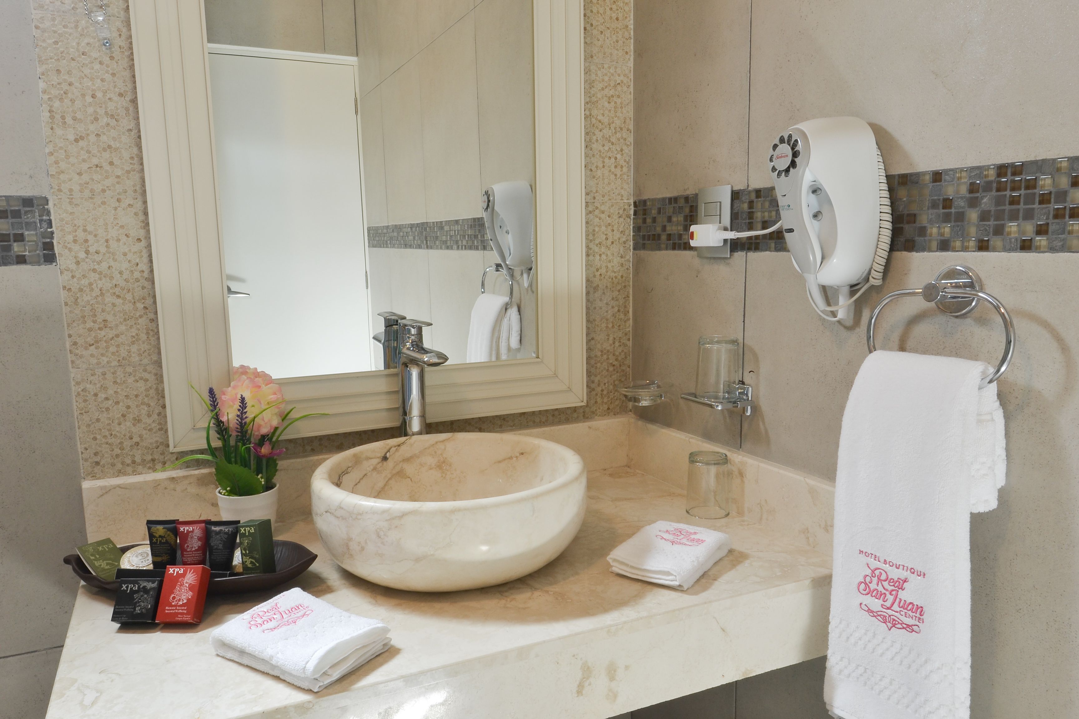 A bathroom with a large sink, a hairdryer, a towel rack, and toiletries on the counter.