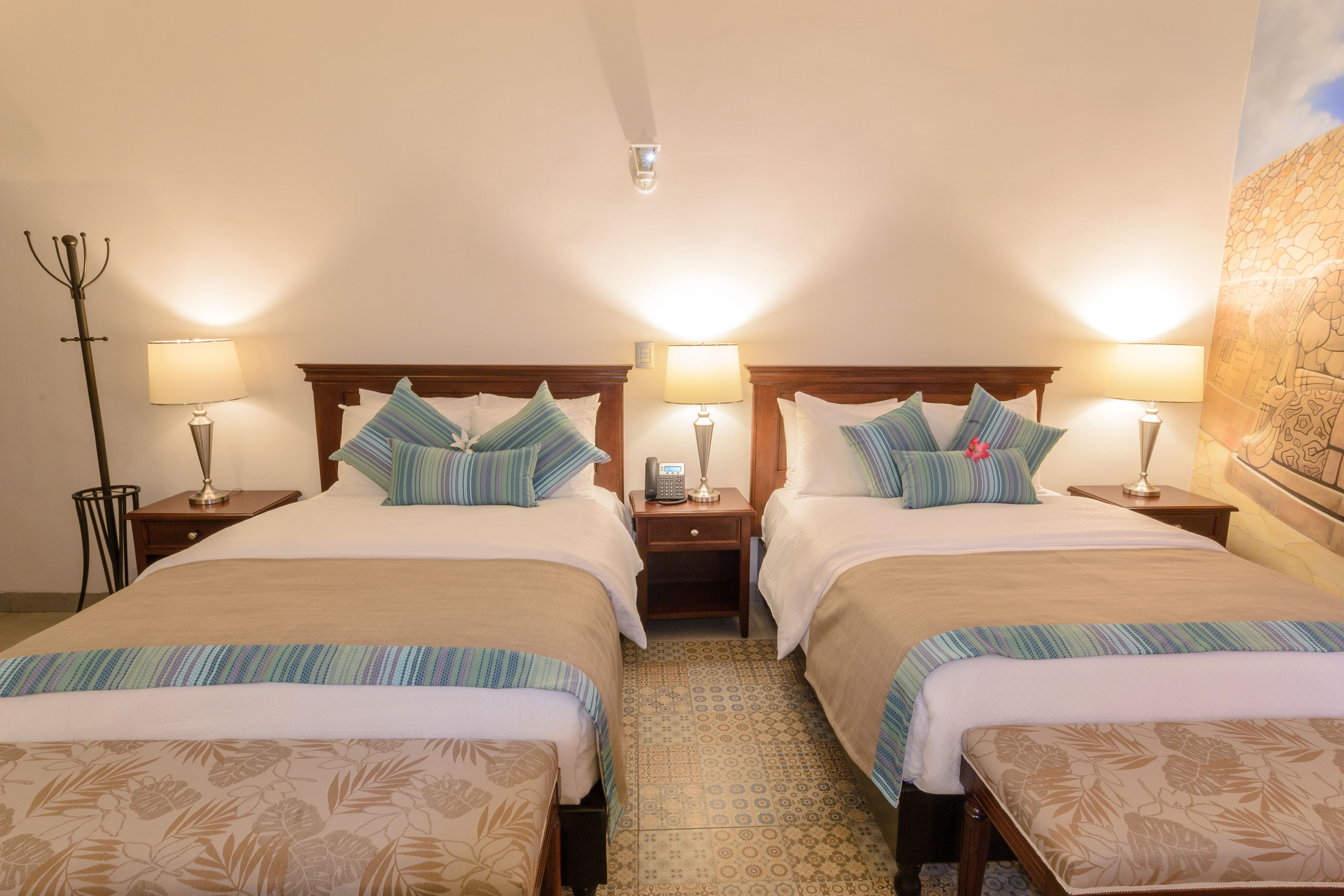 A hotel room with two beds, each with a wooden headboard, bedside lamps, and patterned bedspreads.