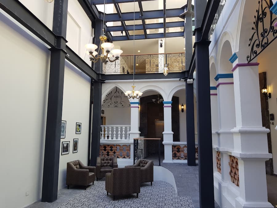 Un patio amplio con techo alto, columnas decoradas y un área de estar con sofás estampados.