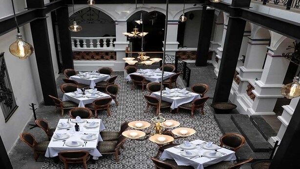 Un restaurante con varias mesas dispuestas para comer, con un suelo estampado y detalles ornamentales en el techo.