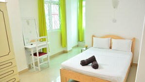 A bedroom with a wooden bed, white pillows, a small bedside table, a chair, and a mirror. - La Primerose (Quatre Bornes)