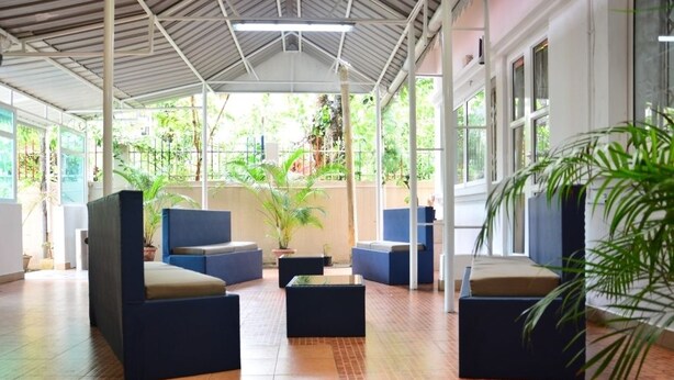 A covered outdoor seating area with blue and beige furniture, potted plants, and a tiled floor. - La Primerose (Quatre Bornes)