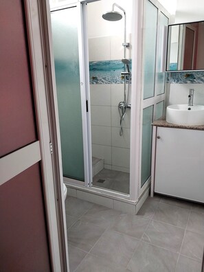 Un baño moderno con ducha acristalada, lavamanos blanco y piso de azulejos.