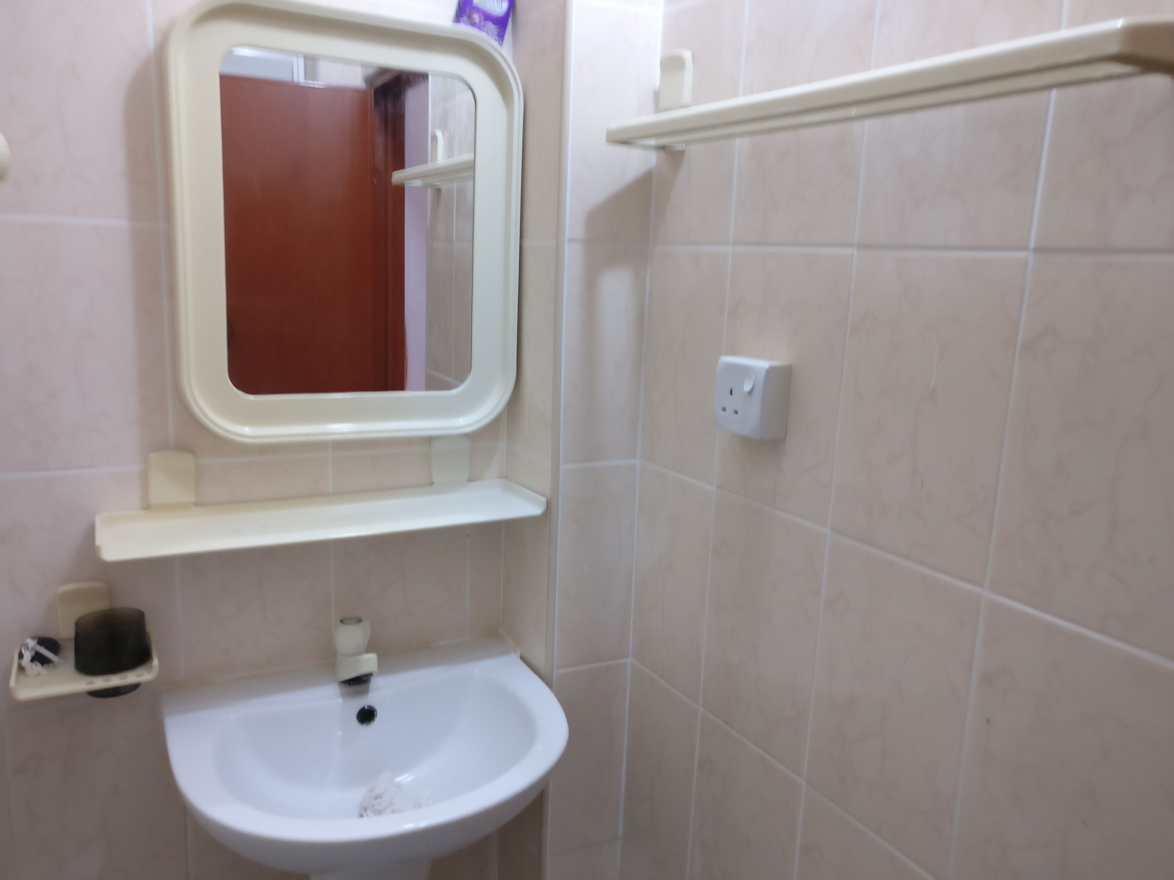 A bathroom with a white sink, a mirror, a shelf, and a towel rack.