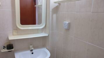 Un baño con un lavamanos blanco, un espejo, una repisa y un perchero para toallas.