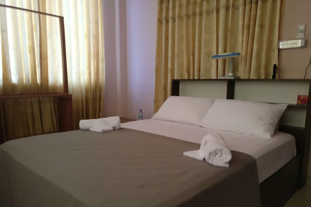 A hotel room with a large bed, a bedside table, a mirror, and a window with curtains.