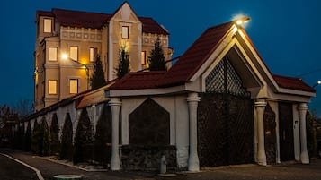A two-story building with a red roof and white walls, featuring a gated entrance and a small fire hydrant in front.