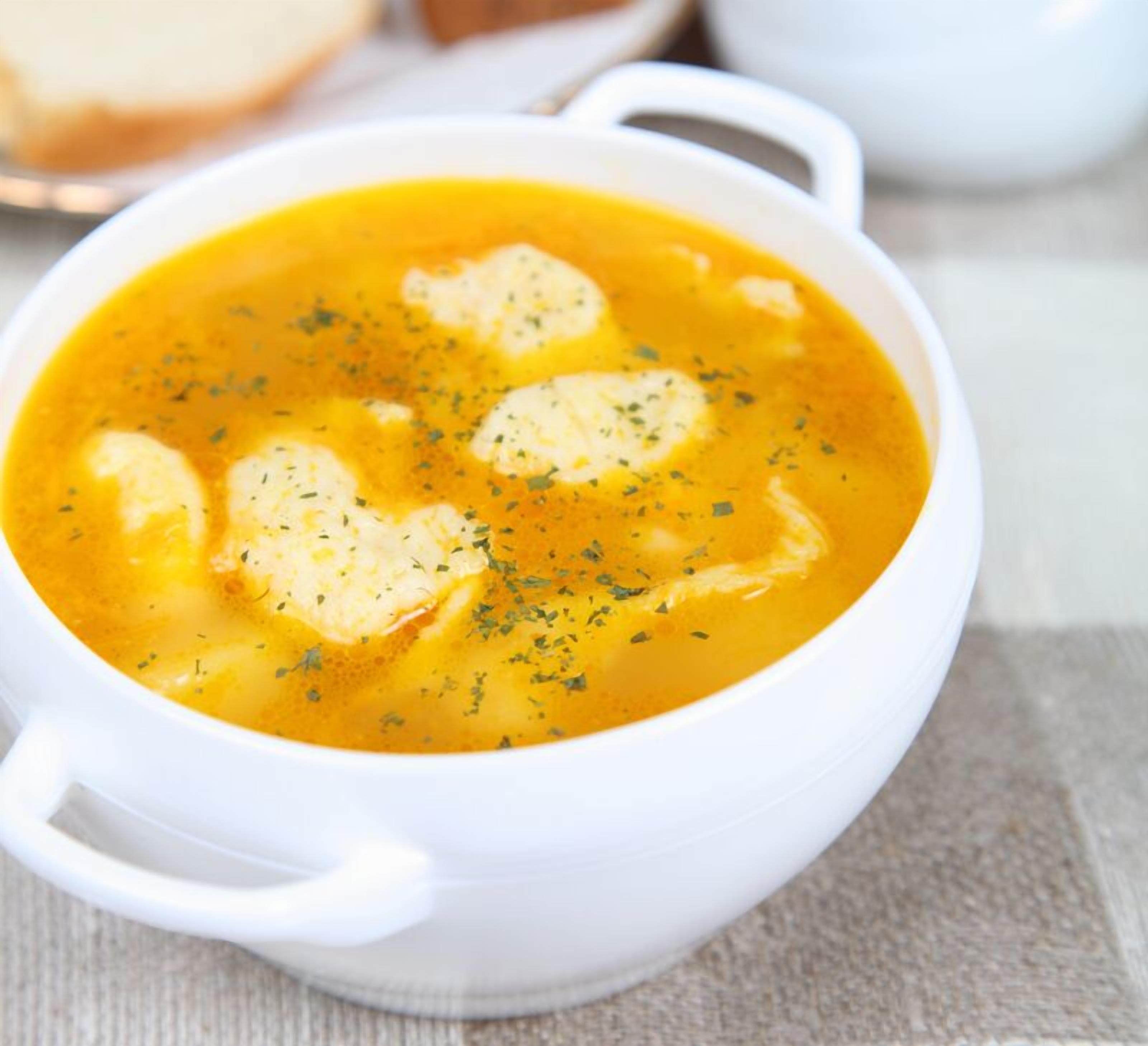 A white bowl of soup with herbs, placed on a table.