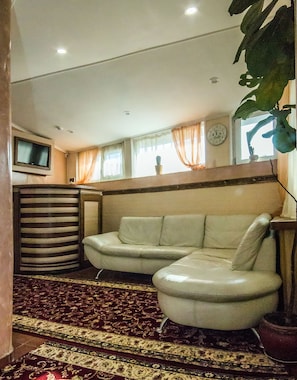 A living room with a sofa, a television, a clock, and a window with curtains. - Velion Hotel (Kharkiv)