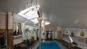 An indoor swimming pool with a tiled floor, a chandelier, and a brick wall. - Velion Hotel (Kharkiv)
