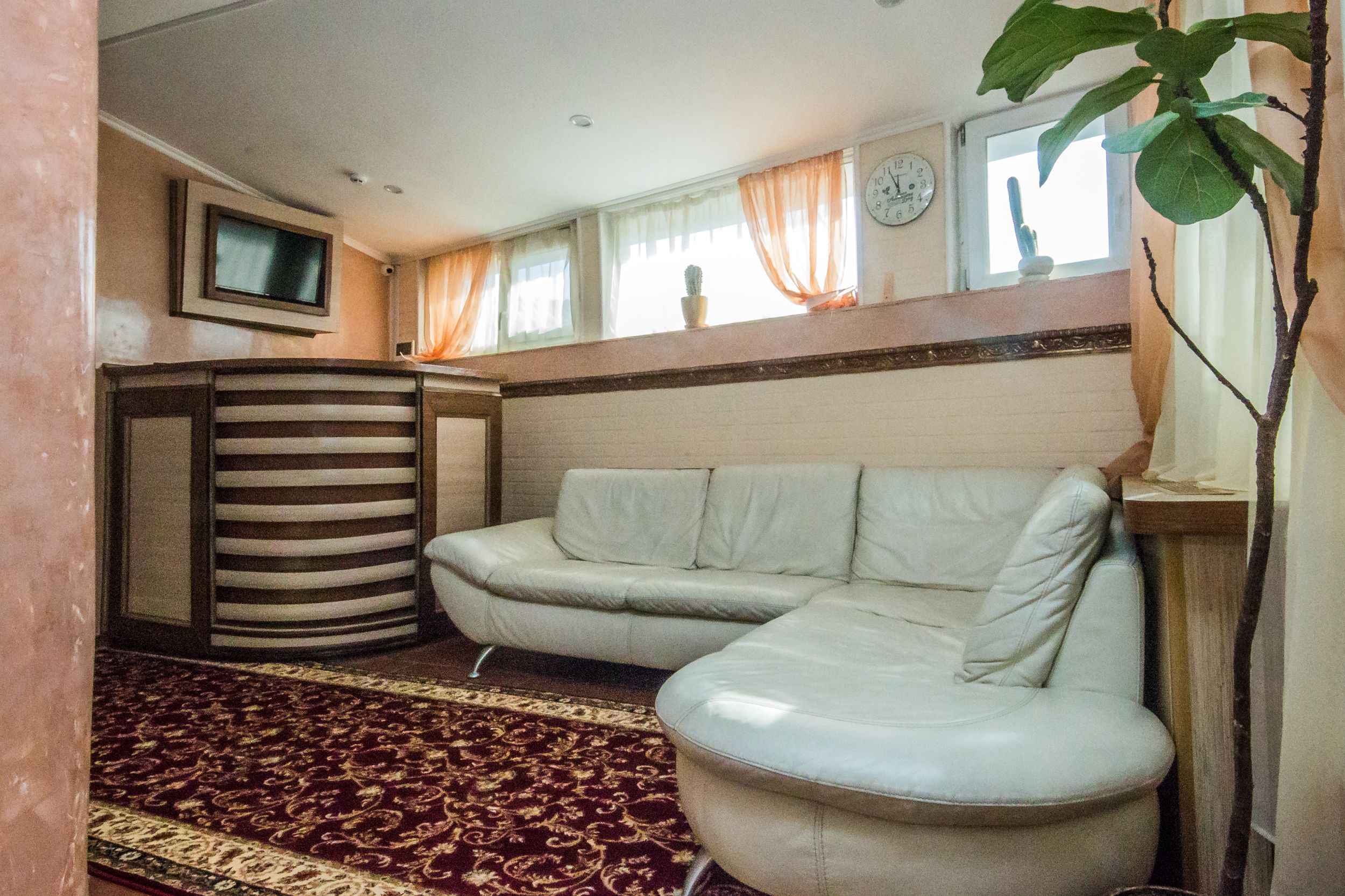 A living room with a sofa, a television, a clock, and a window with curtains.