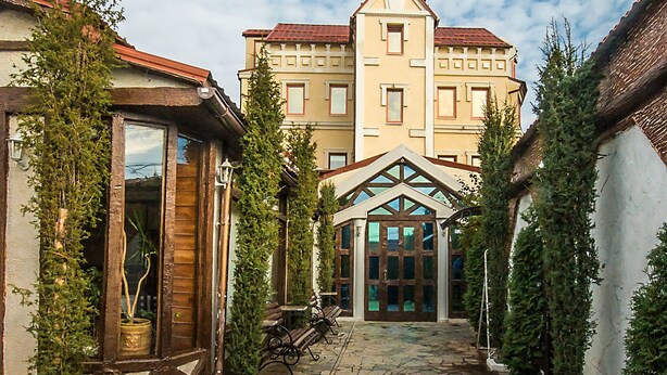 A courtyard with stone paving, wooden benches, and a building with a red roof and multiple windows. - Velion Hotel (Kharkiv)
