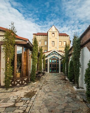 A courtyard with stone paving, wooden benches, and a building with a red roof and multiple windows. - Velion Hotel (Kharkiv)
