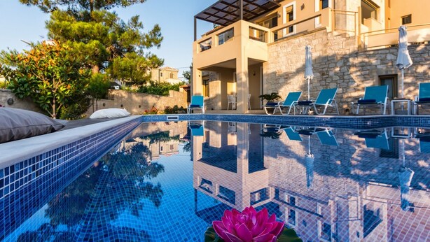 Une piscine ornée d’une fleur de lotus, des chaises longues et un bâtiment en pierre doté d’un balcon.