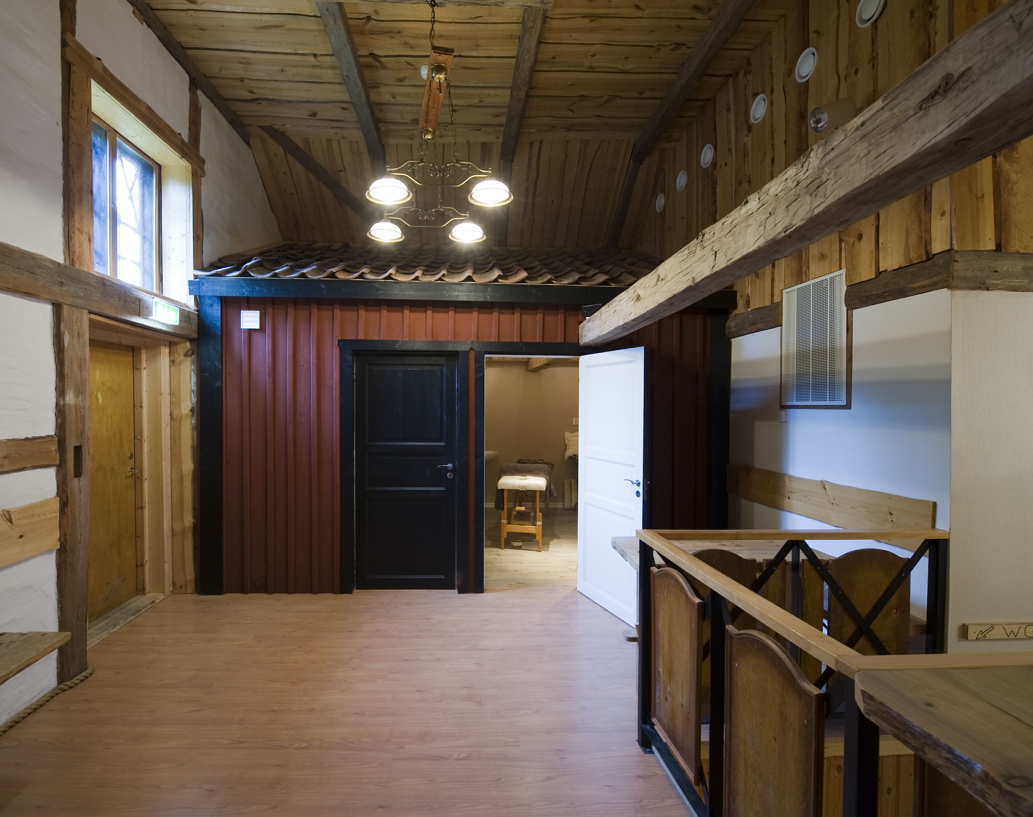 A wooden interior with a hallway leading to a door, a wooden bench, and a ceiling with exposed beams and lights.