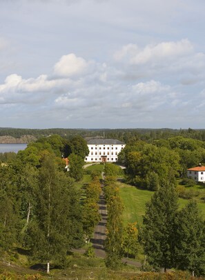 A large white building with a symmetrical facade, surrounded by lush greenery and a clear sky. - Husby Säteri (Soderkoping)