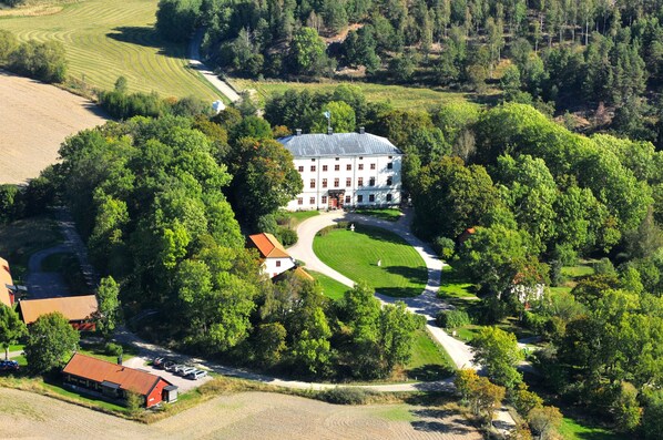 A large, white building with a central courtyard surrounded by lush greenery. - Husby Säteri (Soderkoping)