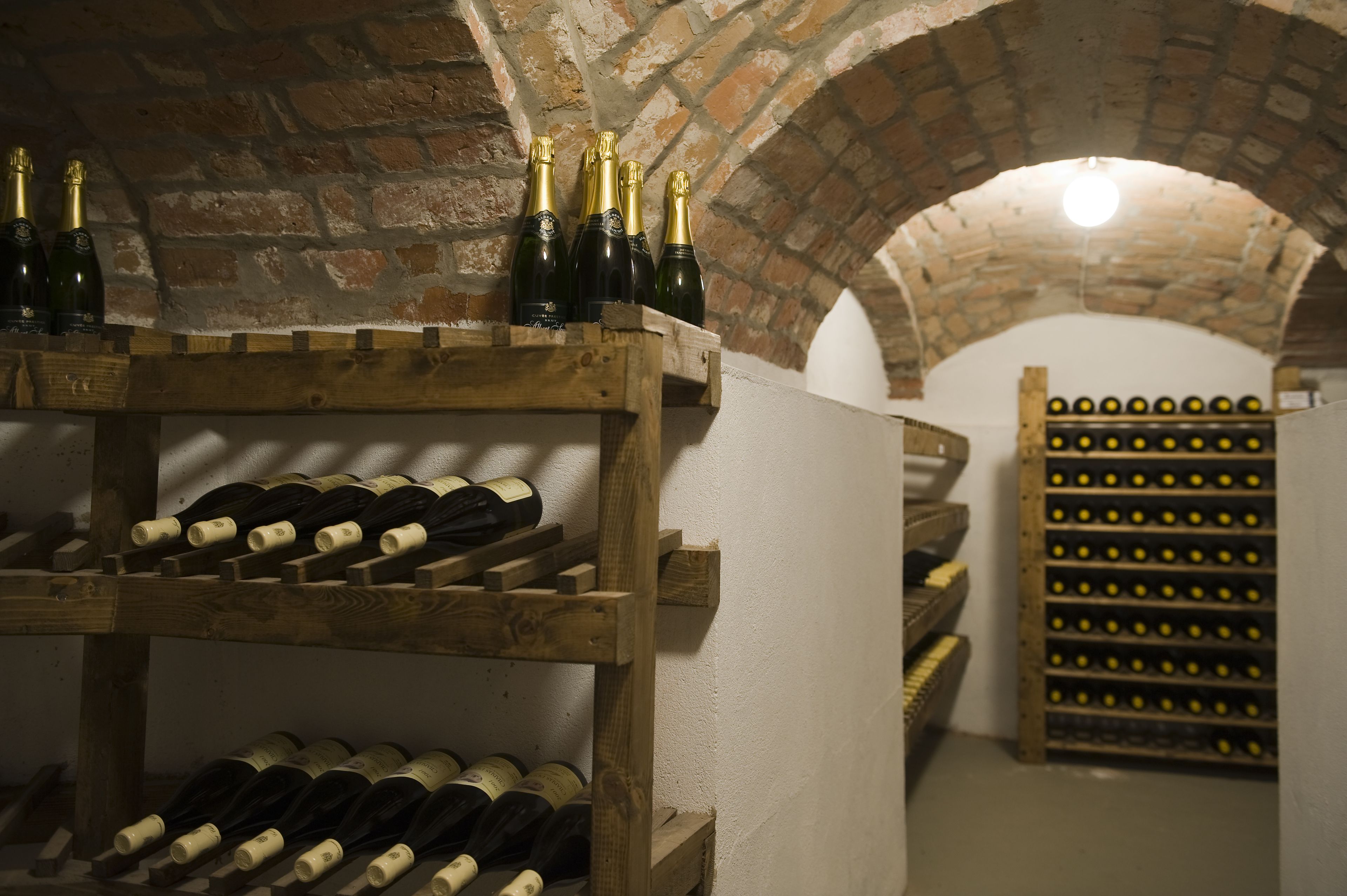 Una bodega con estanterías de madera llenas de botellas y una pared de ladrillo.