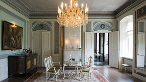 A formal dining room with a chandelier, white chairs, a table, and a patterned rug. - Husby Säteri (Soderkoping)