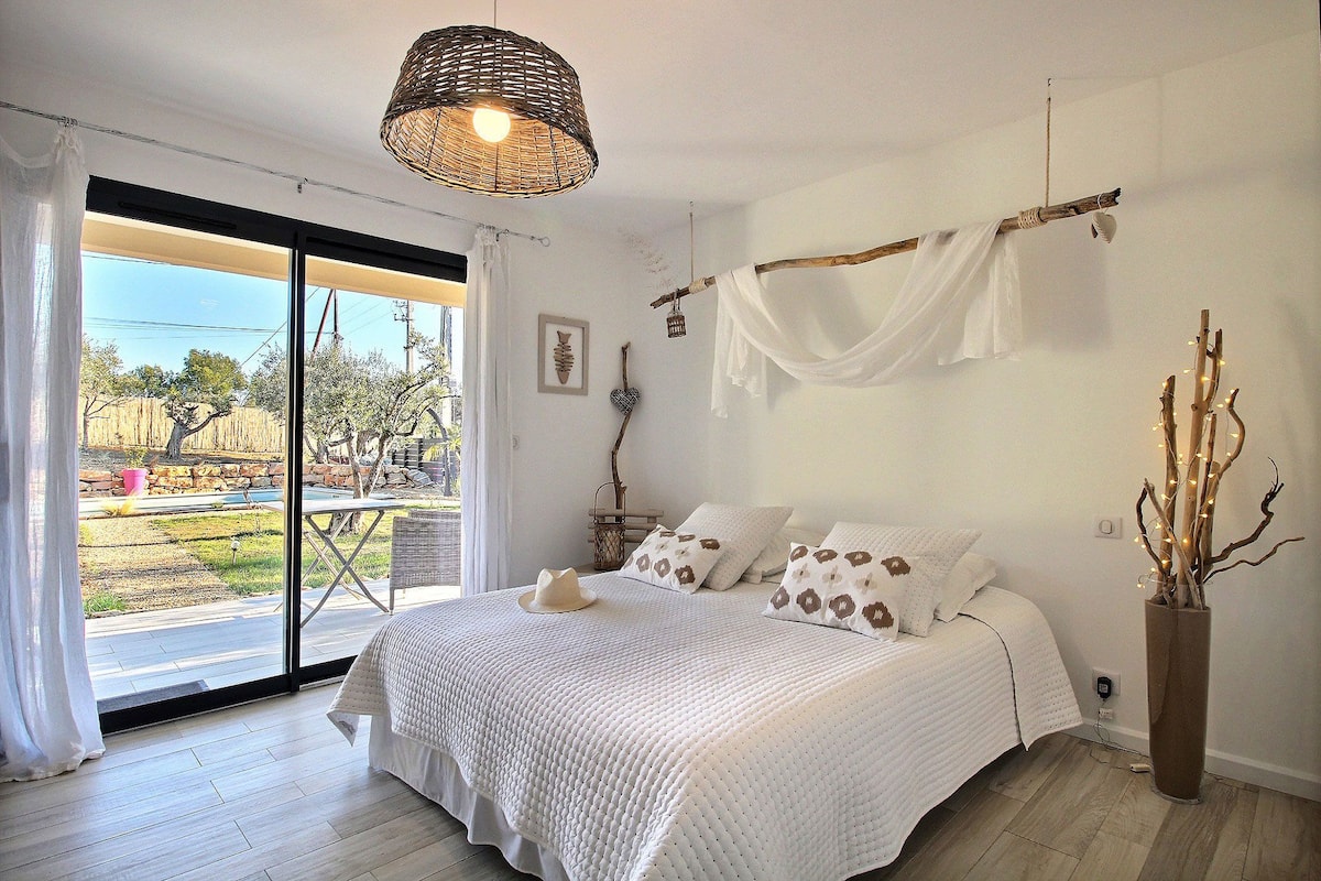 A bedroom with a large bed, a hanging light fixture, a view through a sliding glass door, and a vase with branches.