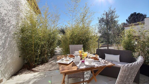 Een terras met een ontbijttafel, omgeven door groen en een rieten bank.