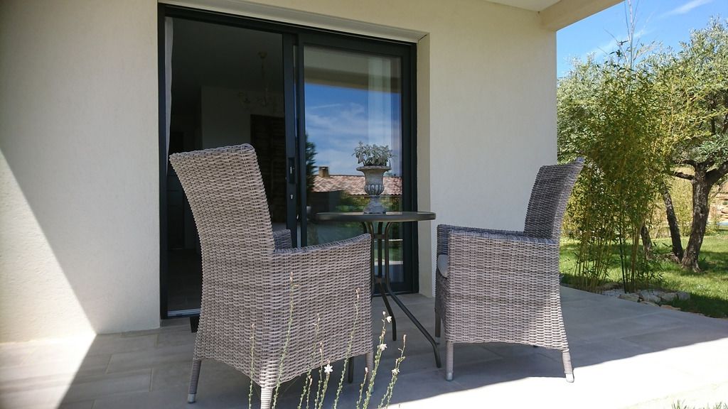A balcony with wicker furniture and a glass door leading to a garden.