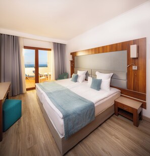 Hotellihuone, jossa on suuri sänky, työpöytä, tuoli ja näkymä rannalle.